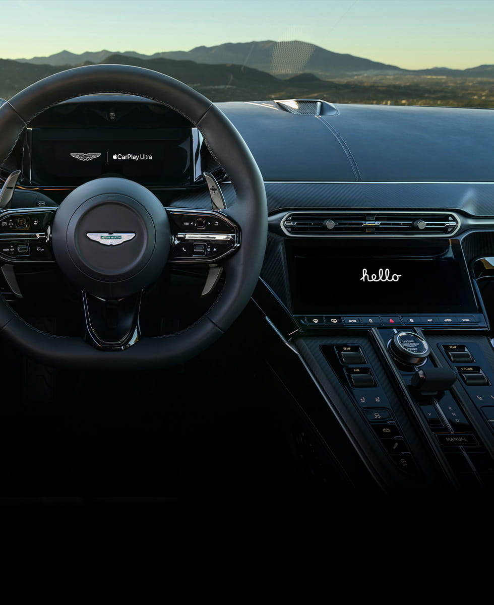 Driver-focused view of a Vantage Coupe interior highlighting the Apple Carplay 2 digital display on both the driver instrument cluster and central touchscreen