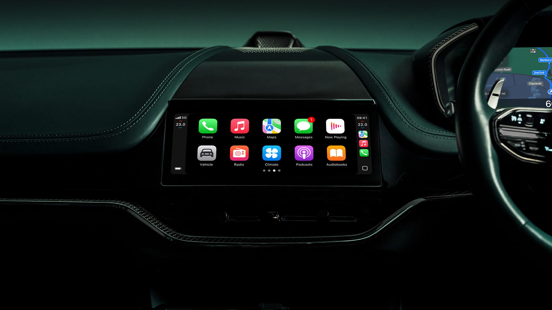 Close-up inside the DBX707 interior showing the centre console touchscreen and a selection of Apple apps including phone, maps, messages, podcasts, vehicle, radio and climate control."